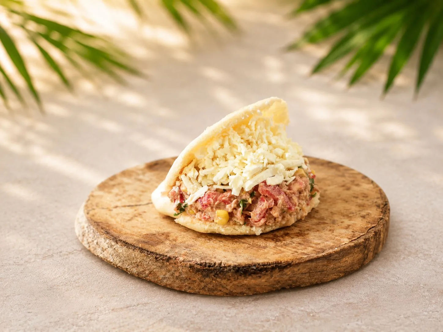 Thunfisch-Arepa (Atún), gefüllt mit Thunfisch und Gemüse, getoppt mit zerbröseltem Hirtenkäse, auf einem Holzbrett.