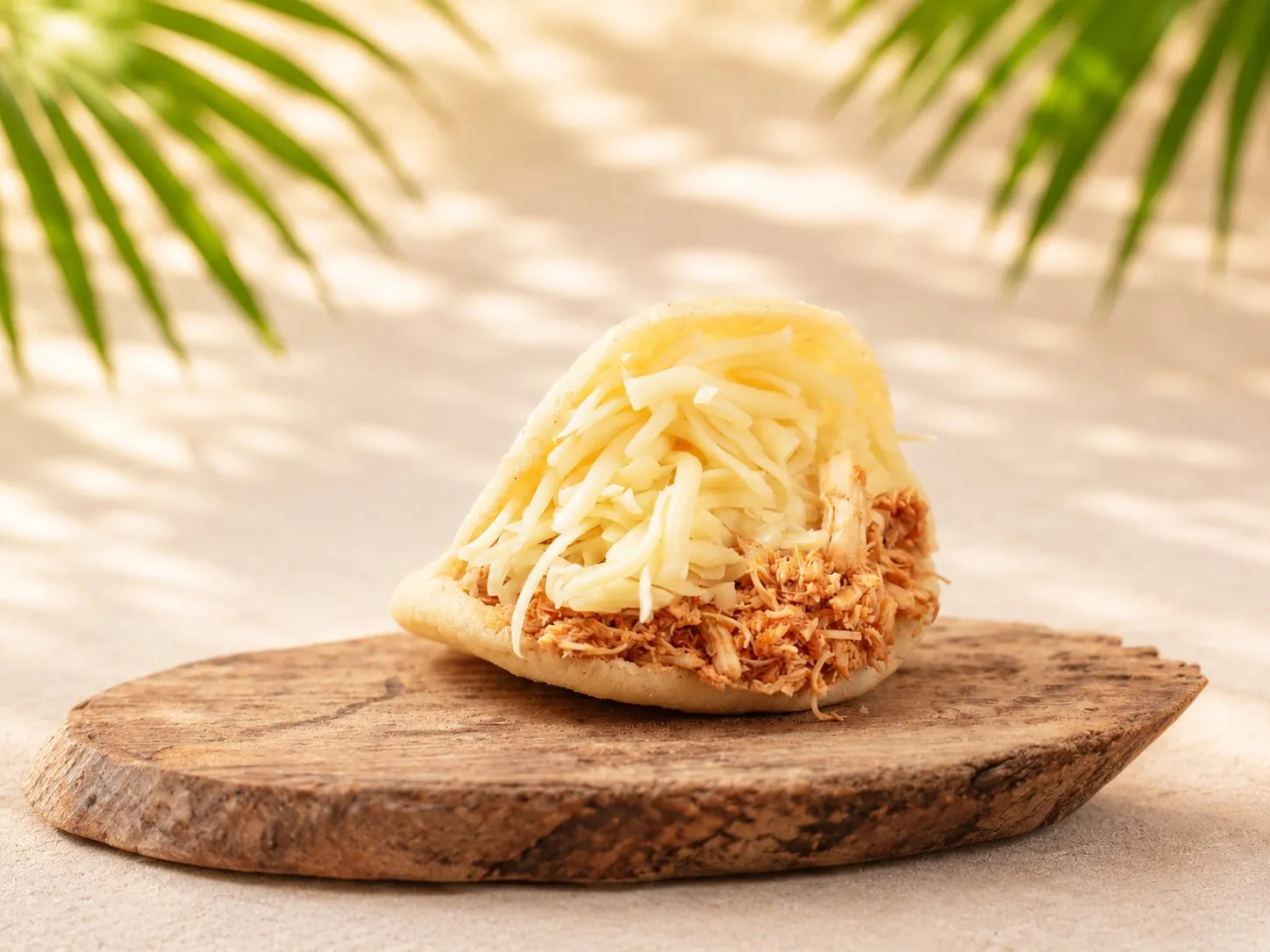 Catira Arepa, gefüllt mit gezupftem Hühnerfleisch und geriebenem Goudakäse, auf einem Holzbrett.