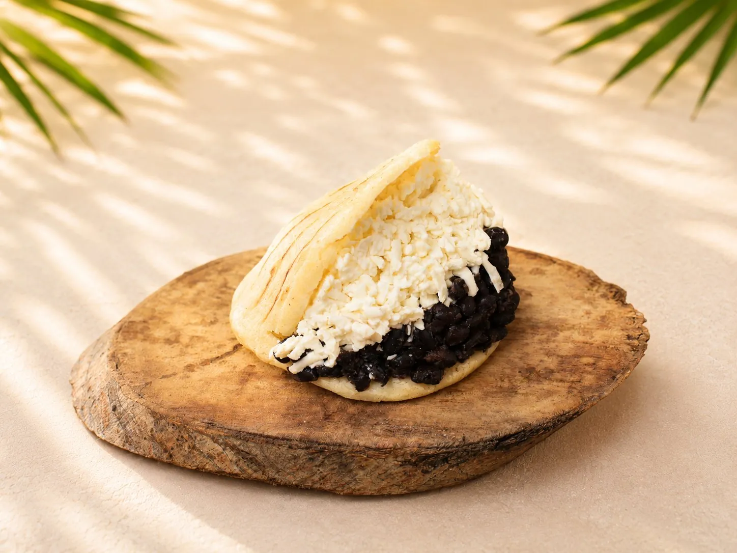 Domino Arepa, gefüllt mit schwarzen Bohnen und zerbröseltem Hirtenkäse, auf einem Holzteller.