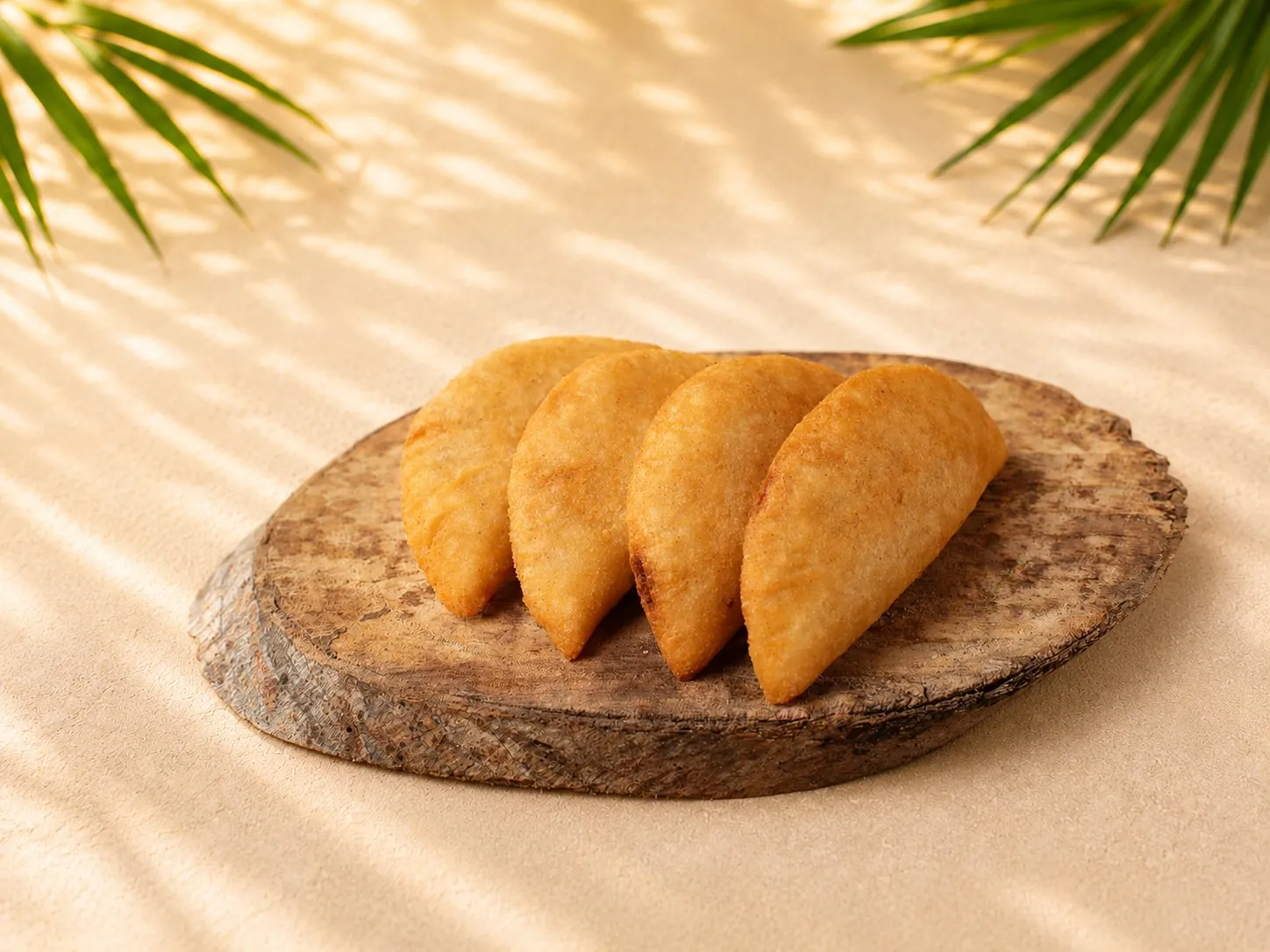 Vier goldbraun frittierte Mini-Empanadas aus Maisteig auf einem rustikalen Holzbrett.