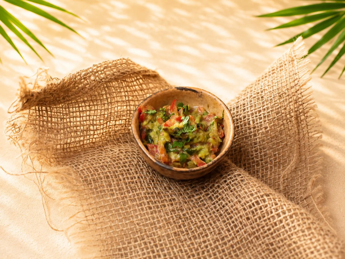 Hausgemachte Guacamole mit groben Stücken von Avocado, Tomate und Koriander in einer kleinen Holzschale auf Jute.