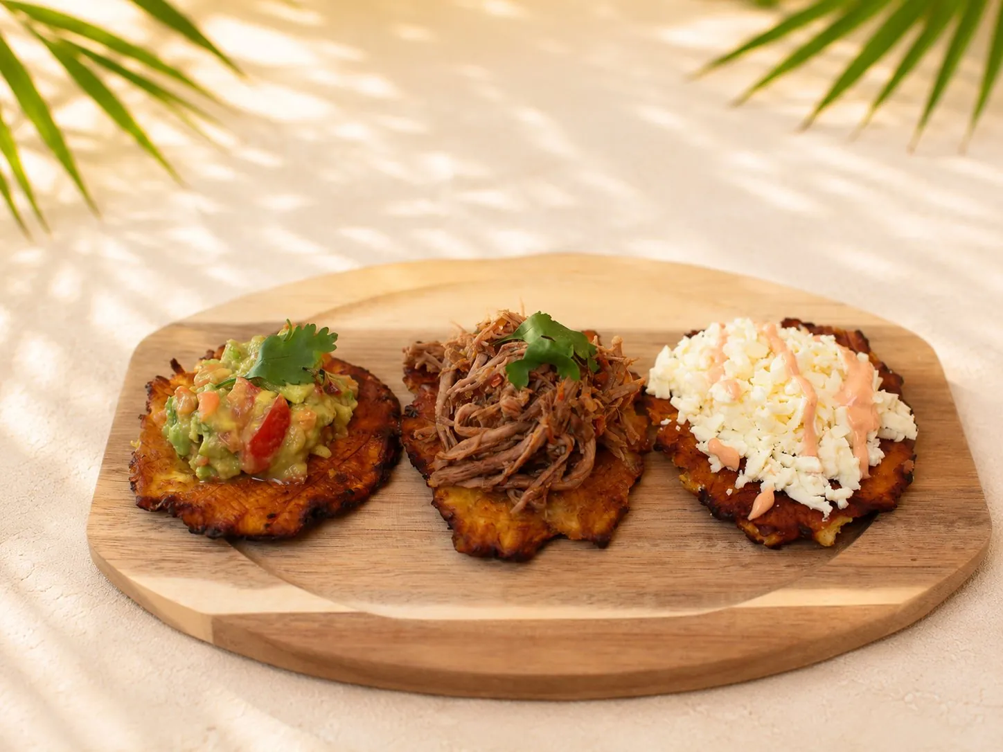 Drei knusprige Tostones aus grünen Kochbananen, belegt mit Guacamole, gezupftem Rindfleisch und Hirtenkäse.